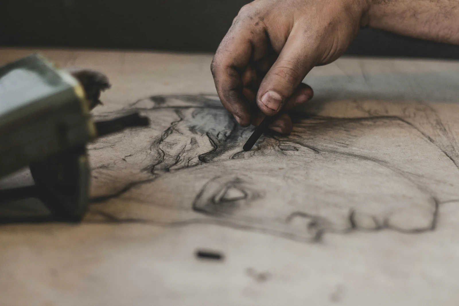 An artist's charcoal-stained hand drawing a face on paper